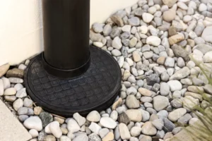 Black metal post with a textured round base set among smooth gray and white stones, seamlessly integrated into an elegant French drain system.